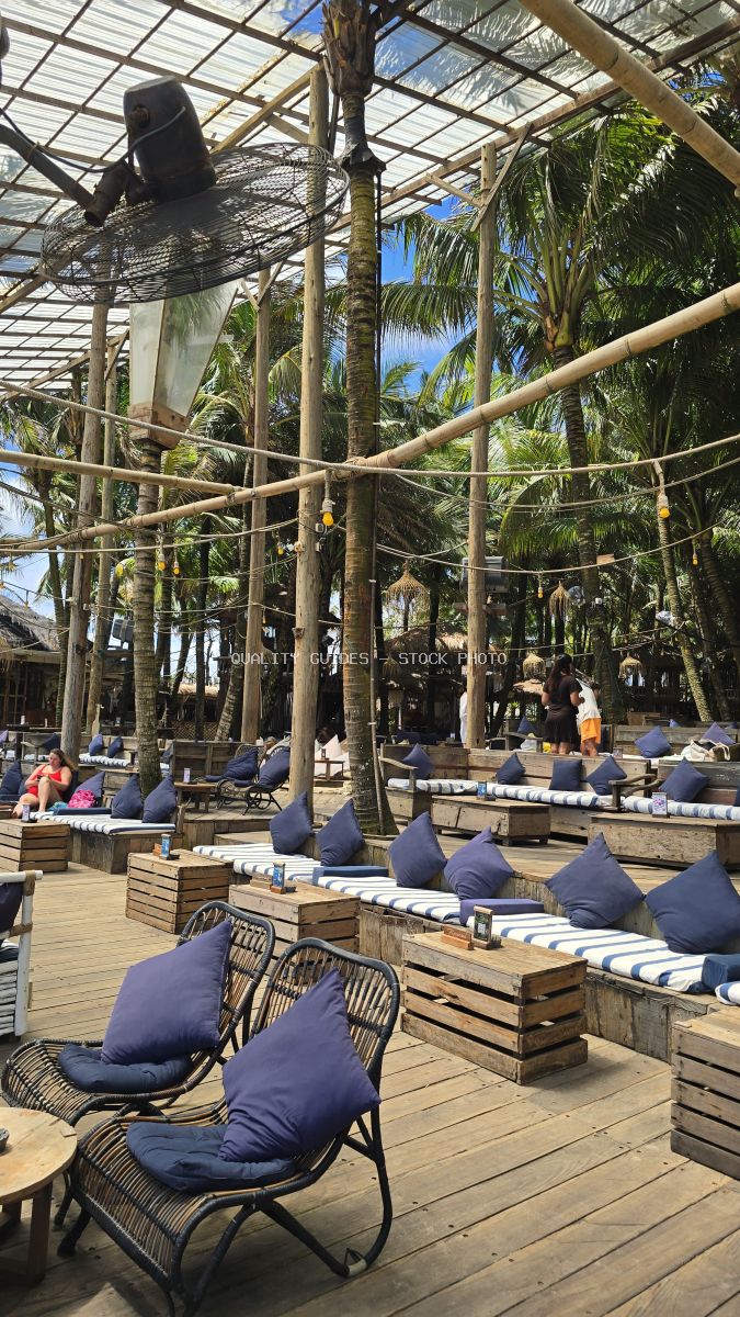 Tropical beach club lounge with navy cushioned seating, wooden pergola, and palm trees in Bali - stock photo