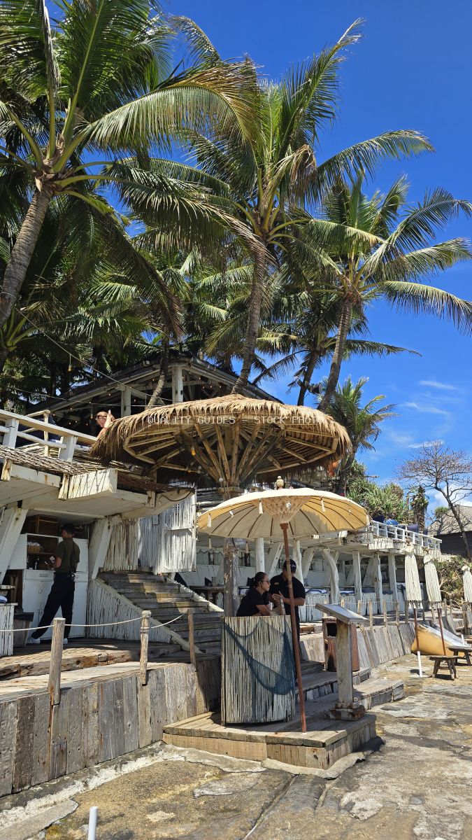 Tropical beach club with thatched umbrellas, wooden structures, and coconut palms in Bali - stock photo