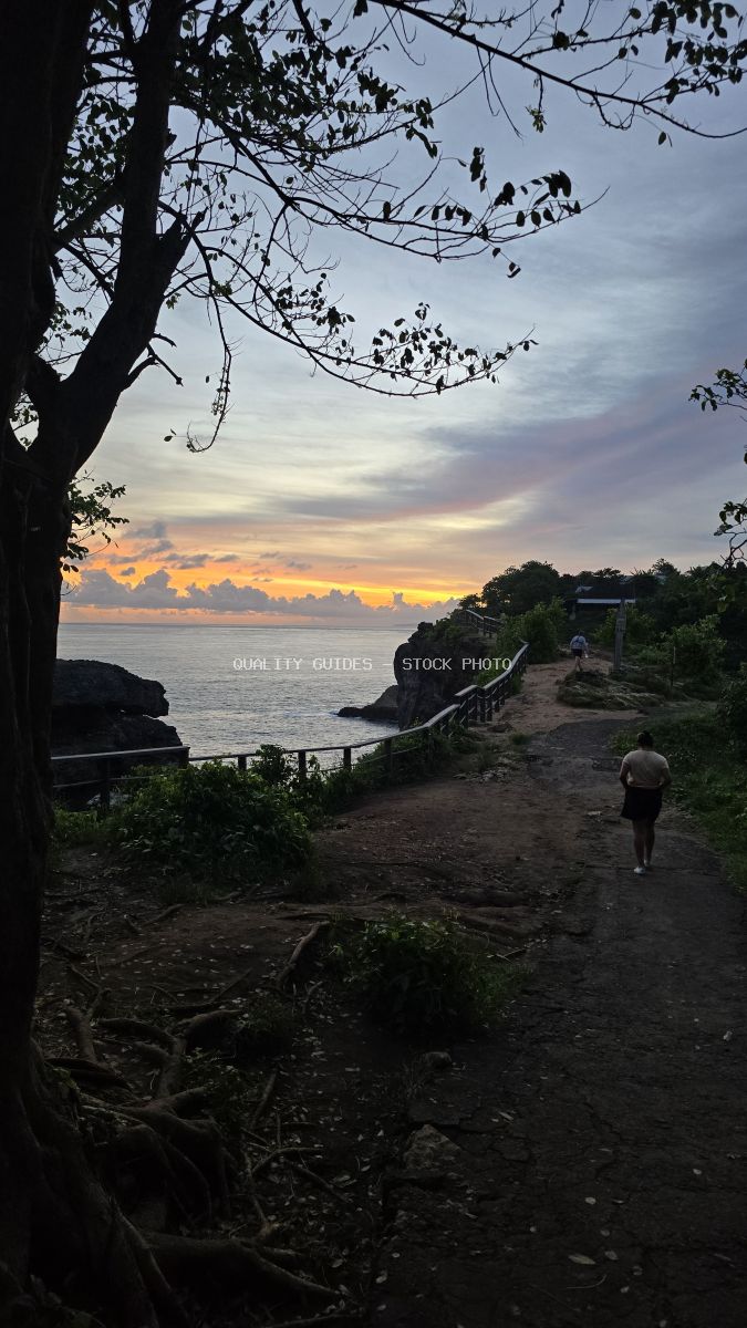 Traveler walking toward sunset at Broken Beach Bali with tropical tree silhouette framing the coastal path - stock photo