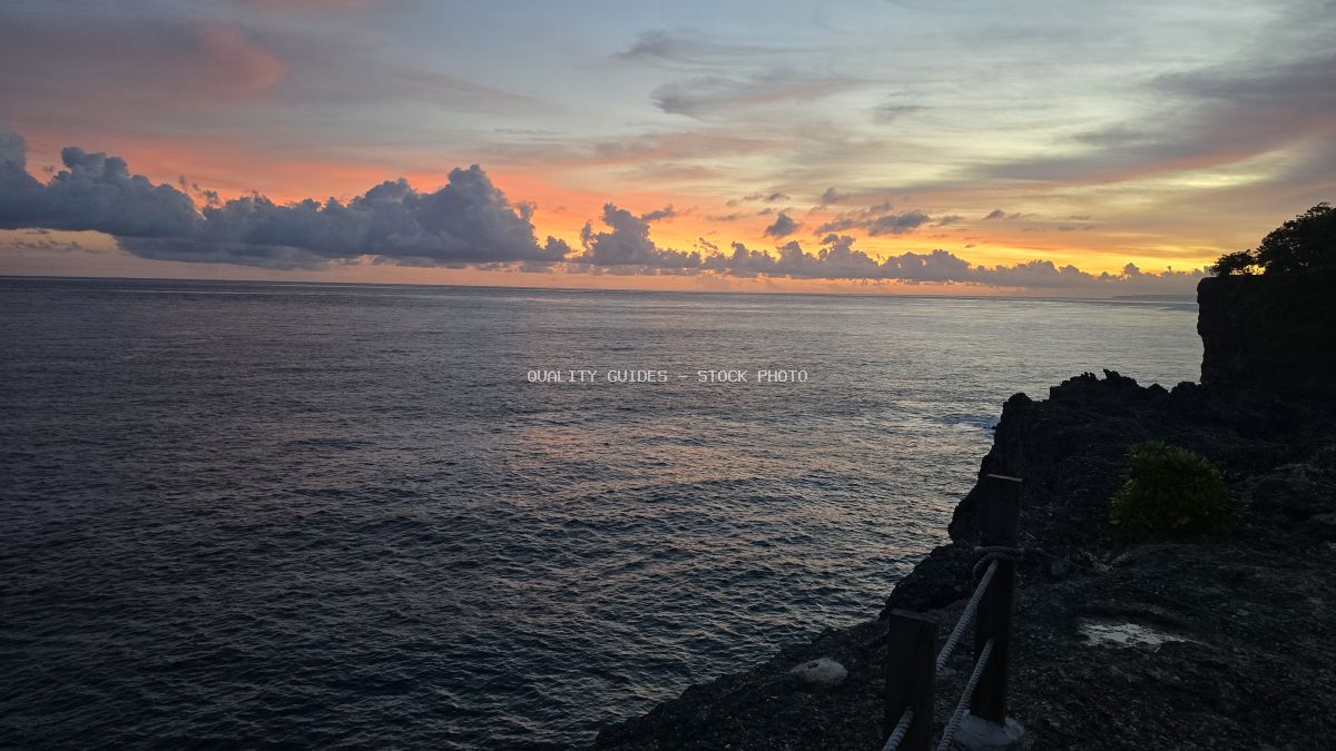 Sunset view from Broken Beach in Bali with dramatic orange sky, volcanic cliffs, and calm ocean horizon - stock photo