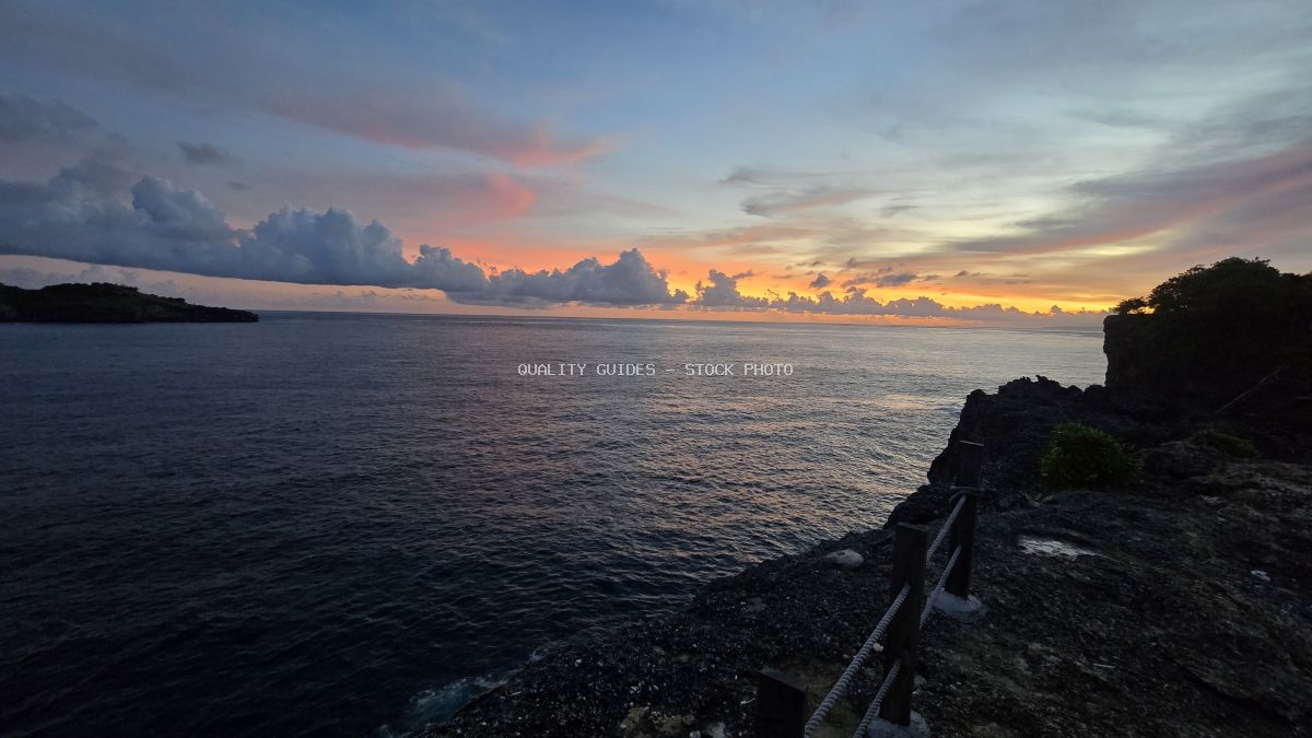 Broken Beach Bali sunset with golden sky, rocky cliffs, and calm ocean waters at dusk - stock photo
