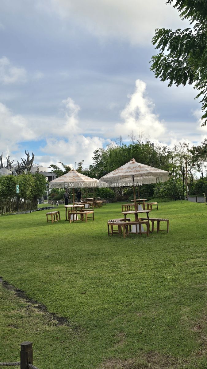 Tropical garden venue with thatched umbrellas and wooden seating on manicured lawn in Bali - stock photo