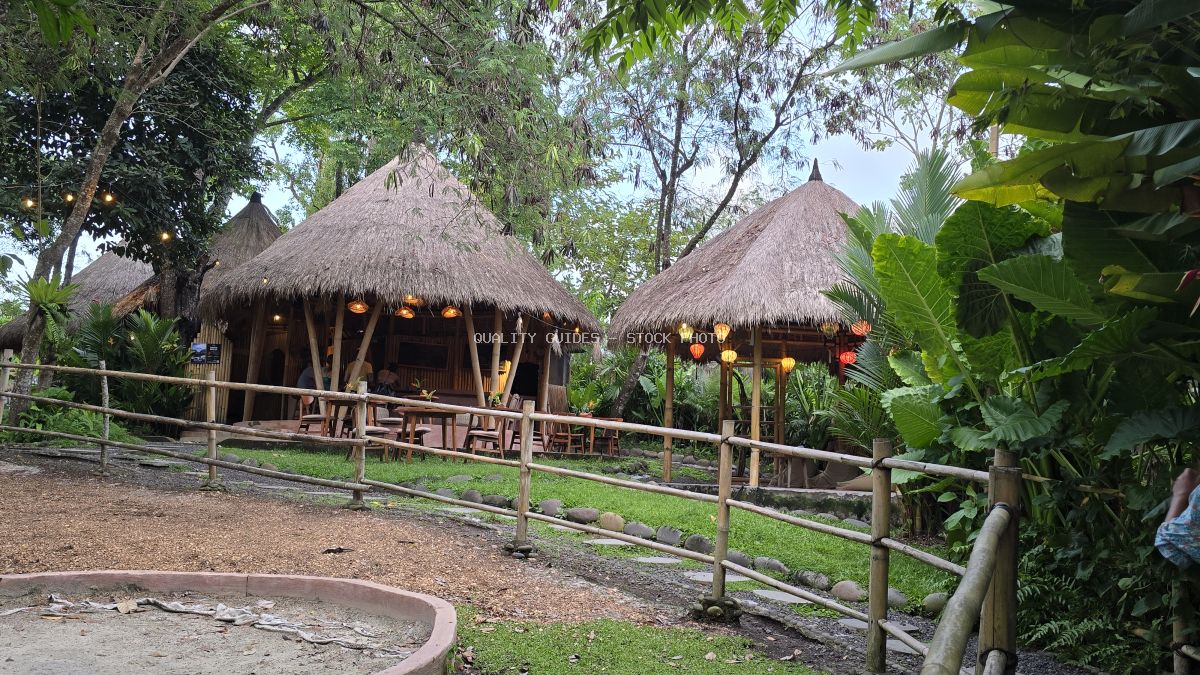 Two traditional Balinese thatched-roof bungalows with colorful lanterns in a tropical garden setting - stock photo