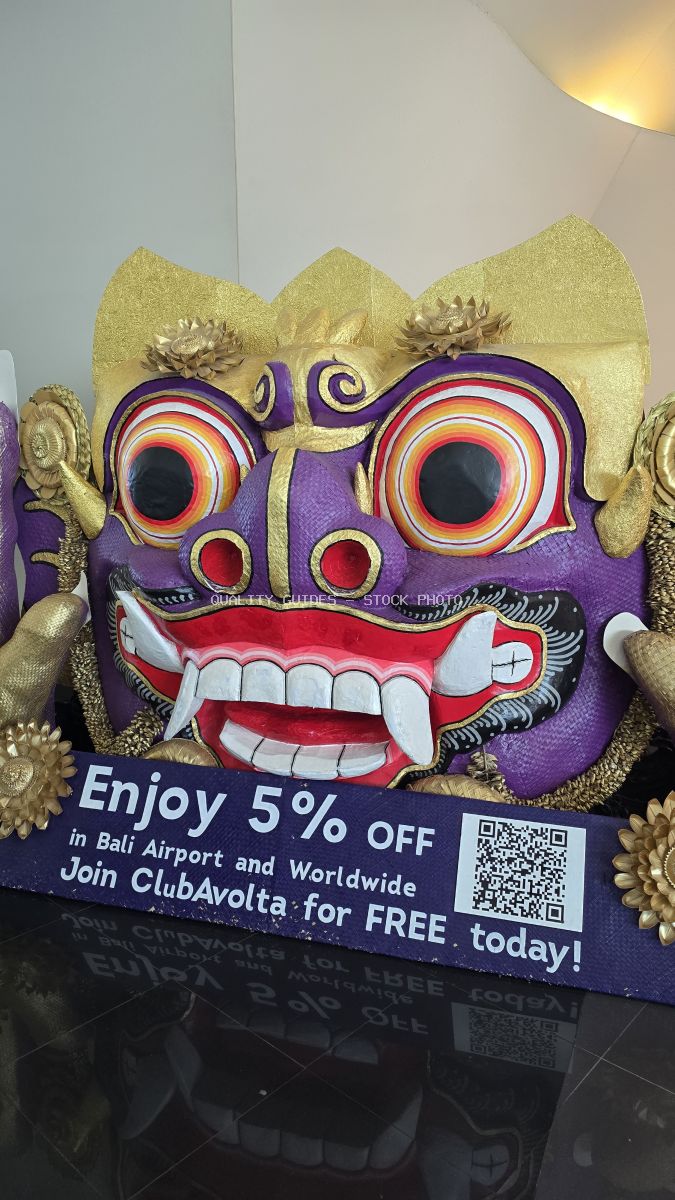 Traditional purple and gold Balinese demon mask with large eyes and white teeth on promotional display at Bali Airport - stock photo