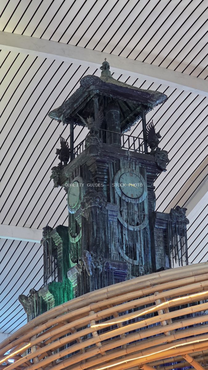 Ornate Balinese clock tower with traditional carvings inside modern airport terminal, Bali - stock photo