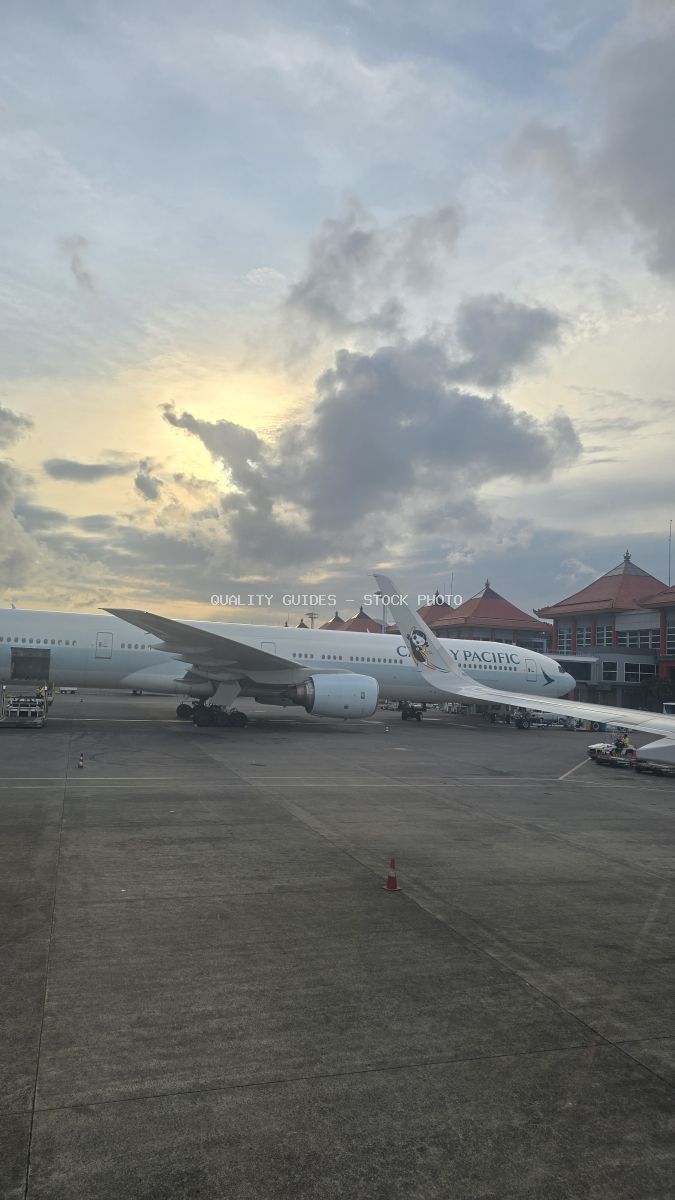 Cathay Pacific airplane parked at Bali airport terminal with red-roofed building and dramatic cloudy sky - stock photo