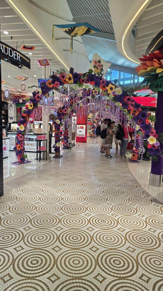 Modern airport terminal with vibrant purple and yellow floral archway installation, geometric floor patterns, and contemporary architecture - stock photo