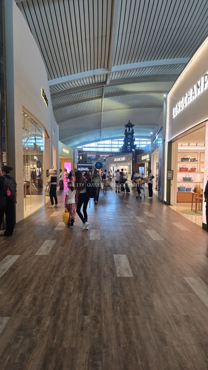 Busy modern airport terminal shopping corridor with ribbed ceiling, retail stores, and travelers walking through Bali International Airport - stock photo
