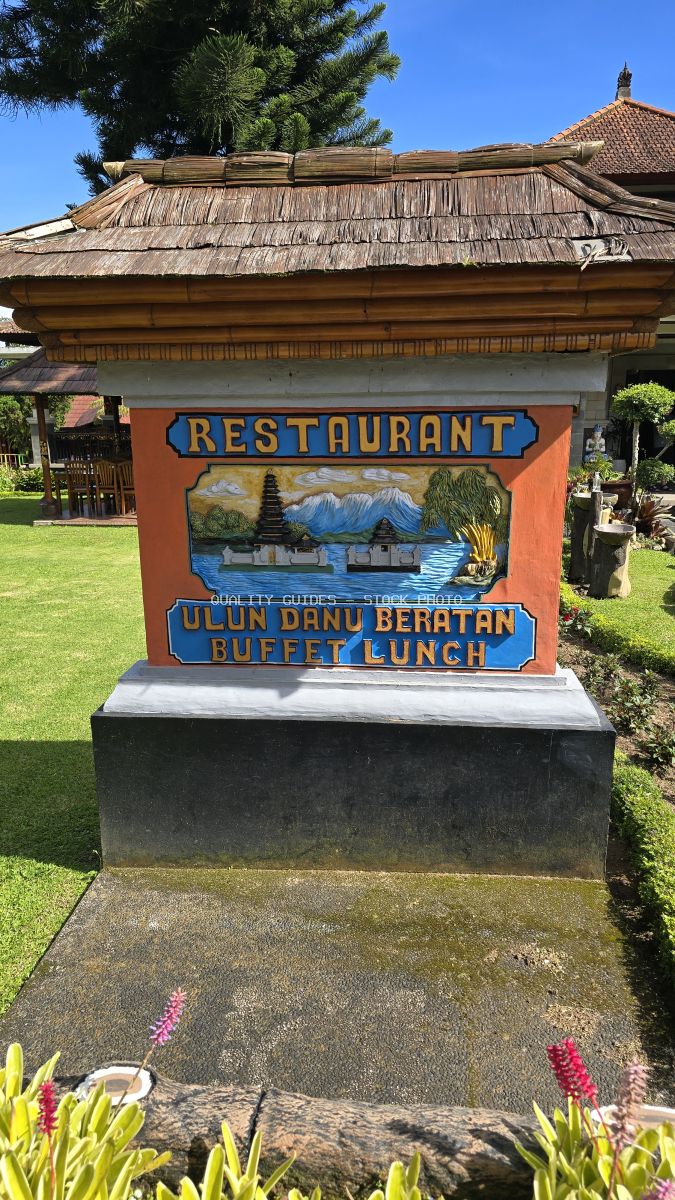 Colorful wooden restaurant sign at Ulun Danu Beratan Temple in Bali with traditional architecture and tropical gardens - stock photo