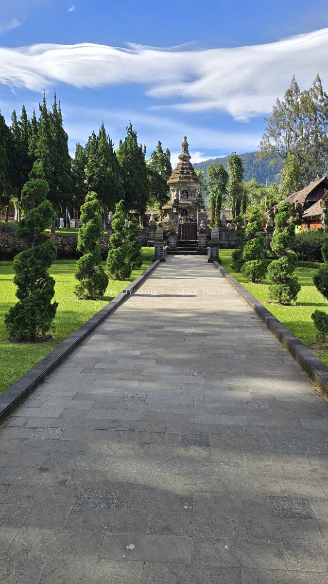 Symmetrical stone pathway leading to Ulun Danu Beratan Temple with cypress trees and mountains in Bali - stock photo