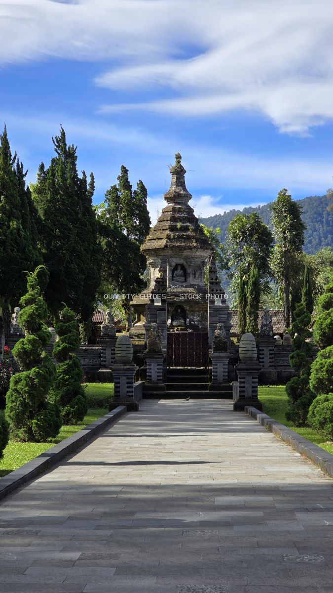 Ulun Danu Beratan Temple in Bali with symmetrical cypress-lined pathway and tiered stone tower against blue sky - stock photo