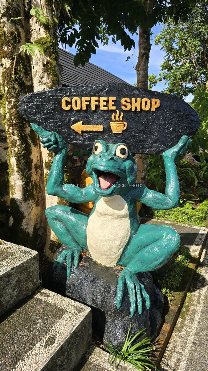 Turquoise frog statue holding coffee shop directional sign in tropical Bali garden - stock photo