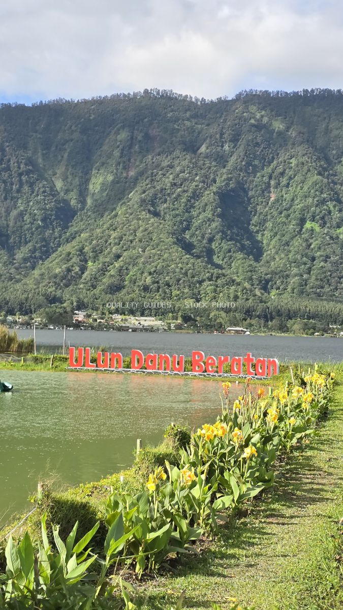 Ulun Danu Beratan Temple with red signage overlooking serene lake and lush green mountains in Bali - stock photo