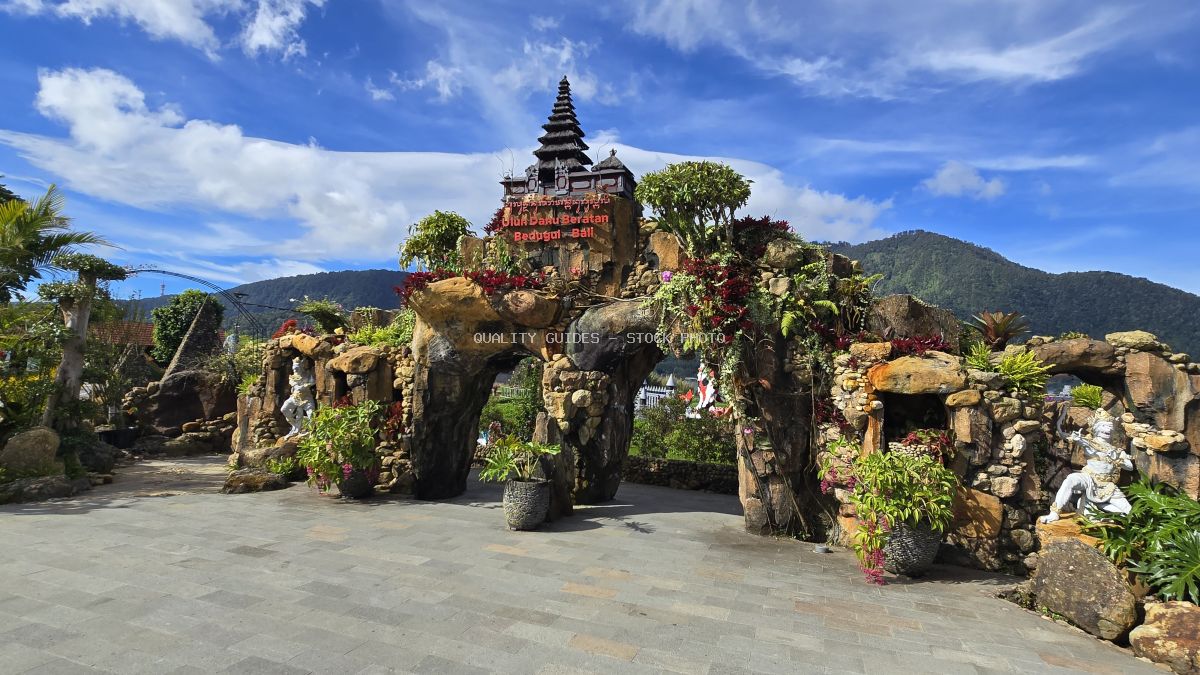 Ornate Ulun Danu Beratan Temple with tiered pagoda roof and decorative stone elephant sculptures adorned with pink flowers, Bali Indonesia - stock photo