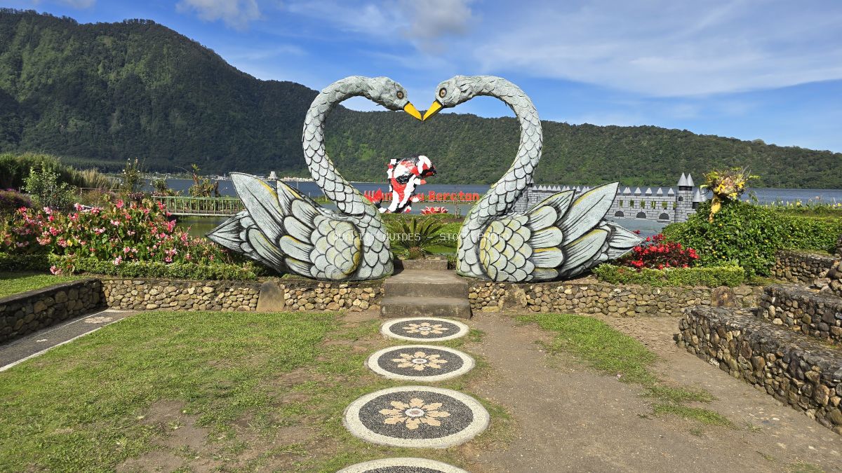 White ornamental swan sculpture forming heart shape at Ulun Danu Beratan Temple with mountain backdrop and lake in Bali - stock photo
