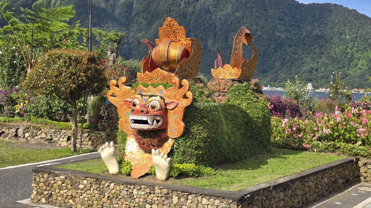 Golden ornate demon statue in Balinese temple gardens with mountains and lake backdrop - stock photo