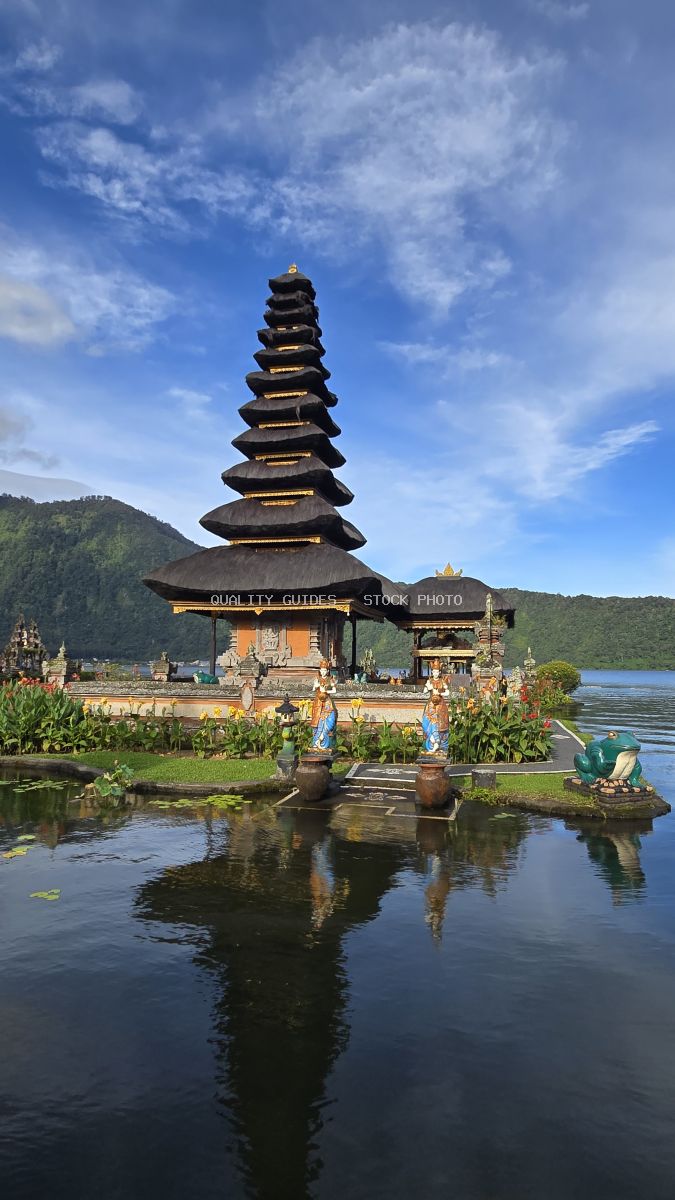 Ulun Danu Beratan Temple with tiered pagoda reflected in Lake Beratan, Bali, surrounded by green mountains and blue sky - stock photo