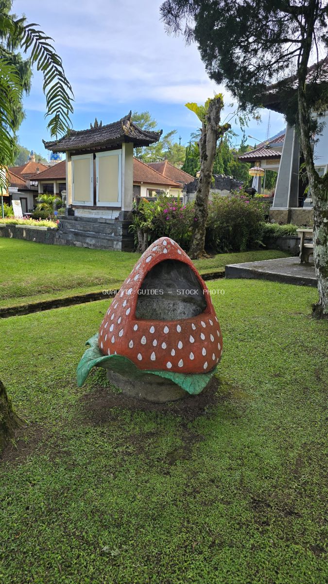 Red and white spotted mushroom sculpture on green lawn at Ulun Danu Beratan Temple in Bali with traditional temple architecture in background - stock photo