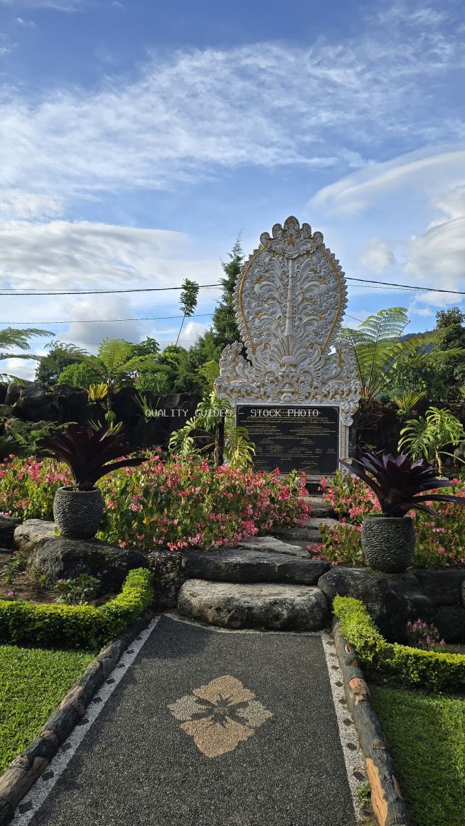 Ornate carved stone monument in tropical Balinese temple garden with pink flowers and palm trees - stock photo