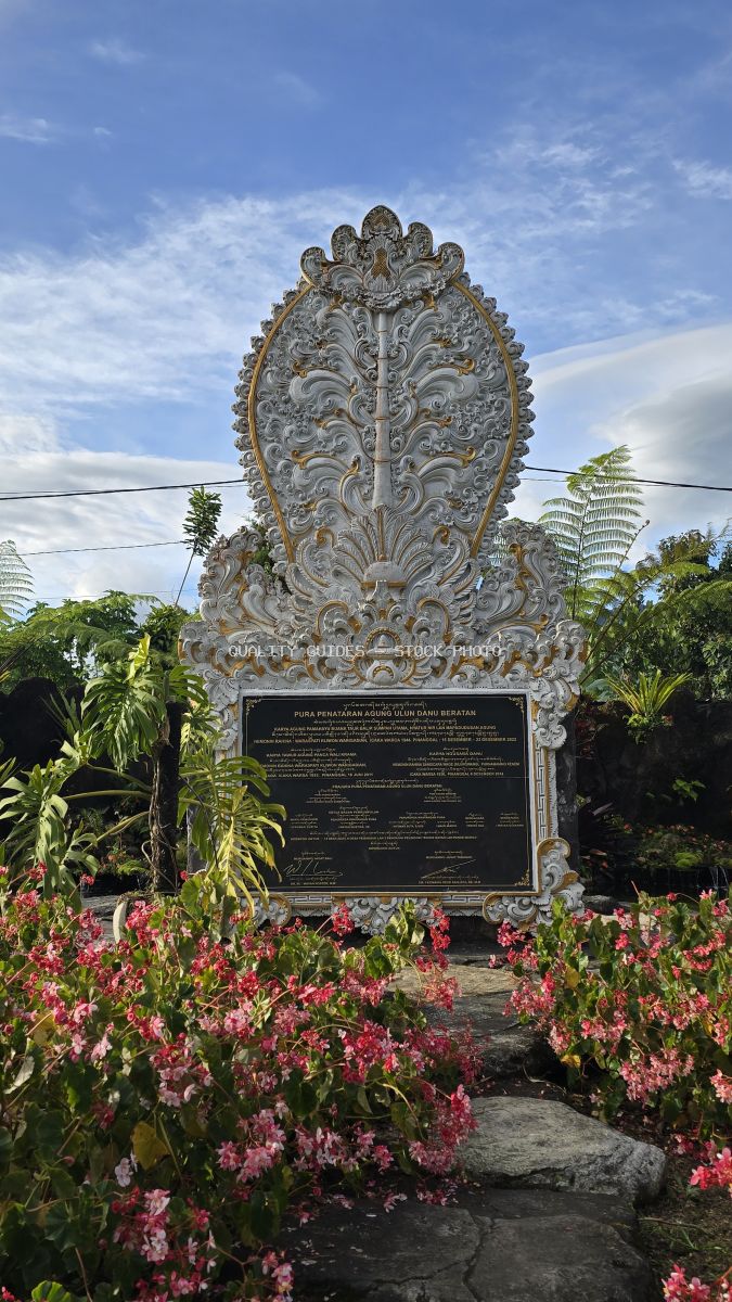 Ornate white stone Balinese monument with intricate carved details surrounded by pink flowers and tropical plants - stock photo