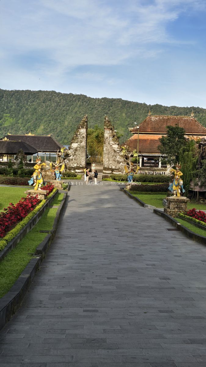 Ulun Danu Beratan Temple in Bali with stone pathway, golden statues, and mountain backdrop - stock photo