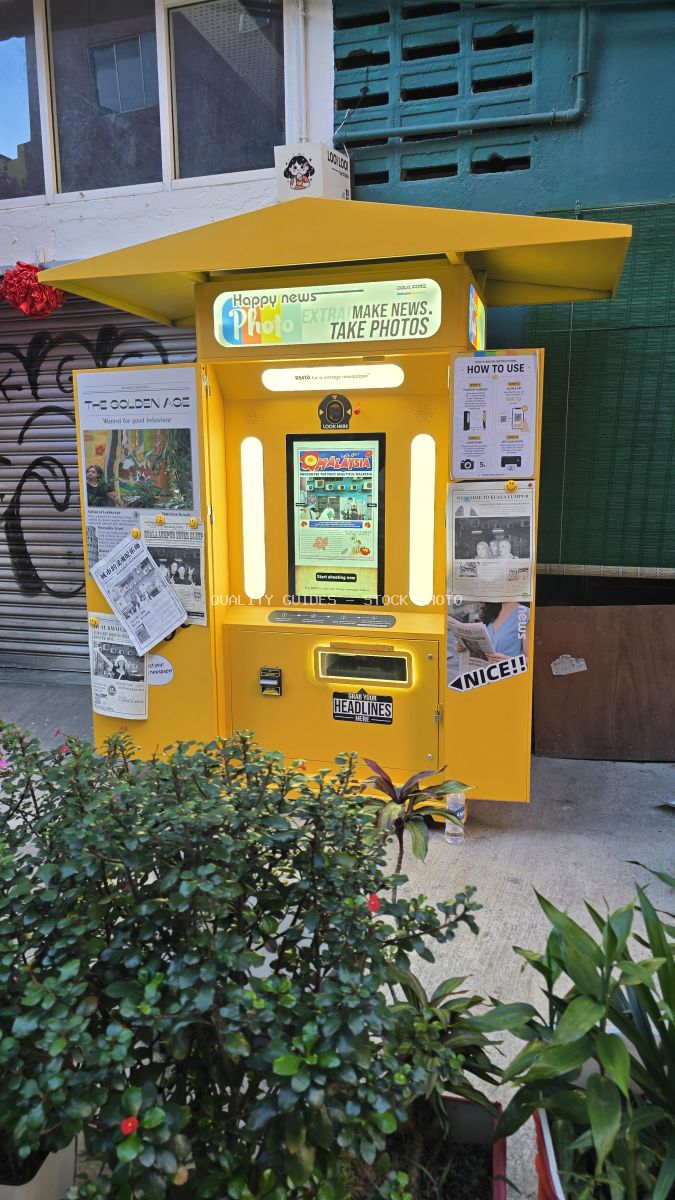 Bright yellow photo booth kiosk with green plants in front of turquoise colonial shophouse at Kwai Chai Hong, Kuala Lumpur - stock photo