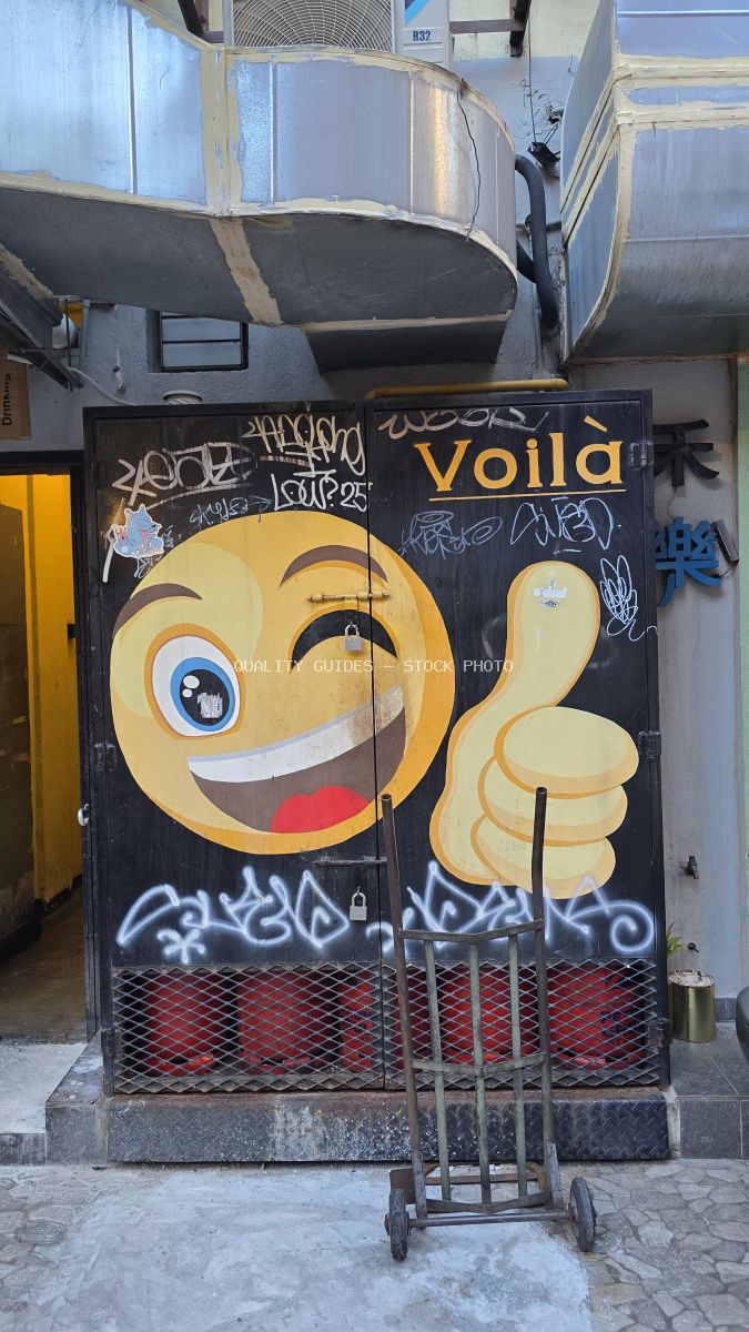 Yellow cartoon character street art mural with thumbs up on black door in Kuala Lumpur alley - stock photo