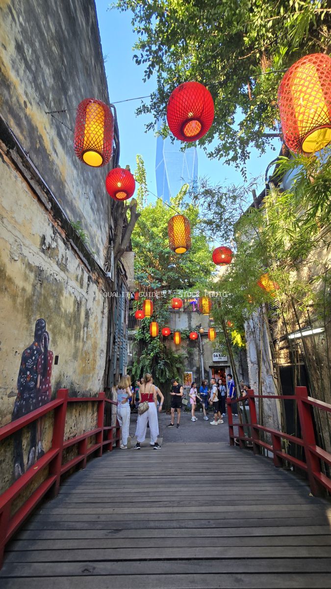Red and yellow lanterns hanging in Kwai Chai Hong heritage alley, Kuala Lumpur Chinatown, with tourists walking through narrow brick passage - stock photo