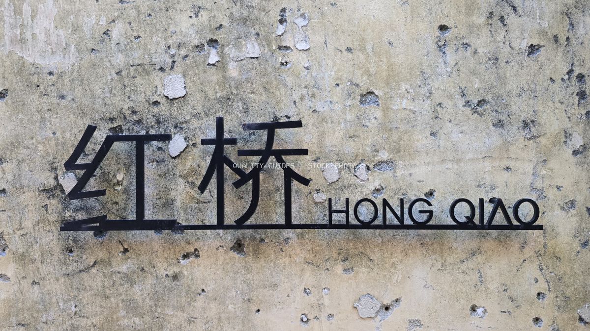 Weathered concrete wall with bilingual Hong Qiao street sign in Chinese and English characters, showing aged paint and texture - stock photo