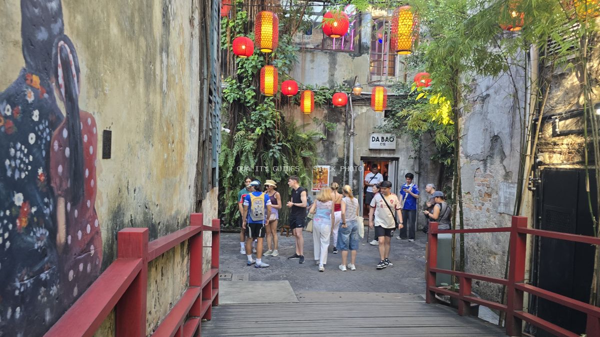 Tourists walking through Kwai Chai Hong alley in Kuala Lumpur with red lanterns and Chinese street art - stock photo