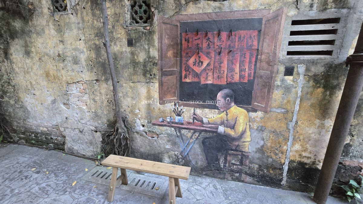 Street art mural of calligrapher in yellow shirt on weathered wall in historic Asian alley - stock photo