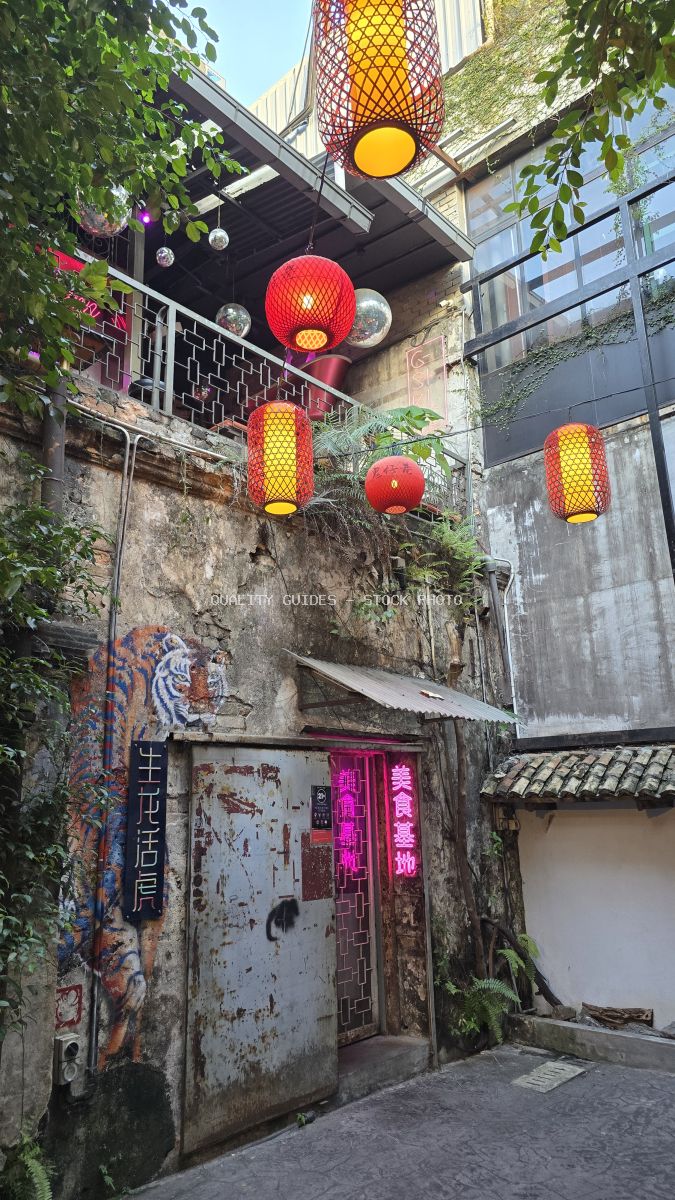 Colorful red and yellow lanterns hanging in a historic alley with weathered walls and green ivy at Kwai Chai Hong, Kuala Lumpur - stock photo