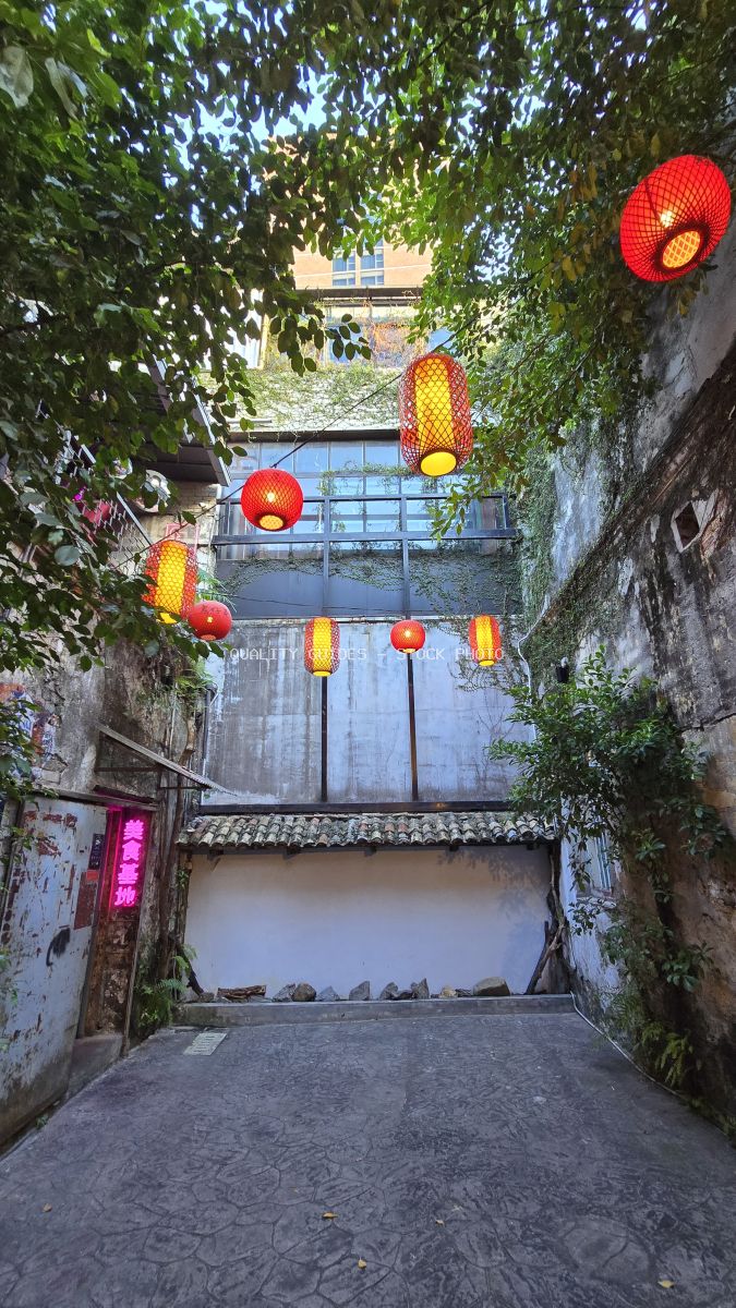 Red and yellow lanterns hanging in a lush green ivy-covered alley with traditional Asian architecture - stock photo