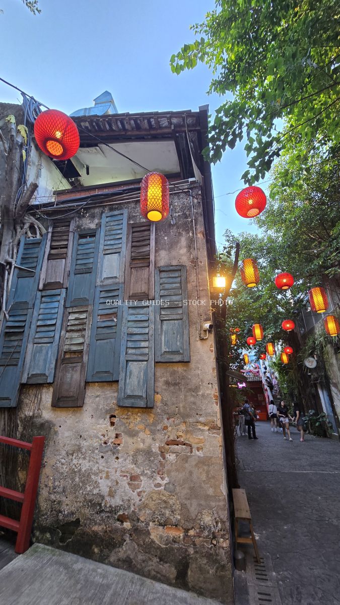 Red and yellow lanterns hanging above a historic alley with blue wooden shutters and aged stone walls in Kwai Chai Hong, Kuala Lumpur - stock photo