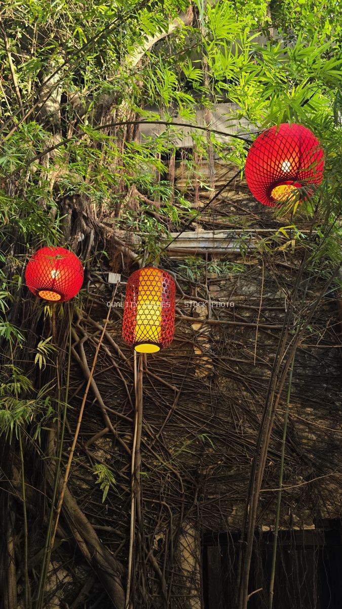 Red lanterns glowing among tropical green foliage and bamboo in a Southeast Asian garden setting - stock photo